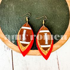 a pair of red and gold football shaped earrings sitting on top of a blackboard