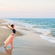 a woman standing on top of a sandy beach next to the ocean with her arms in the air