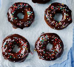 six chocolate donuts with sprinkles on them sitting on top of wax paper