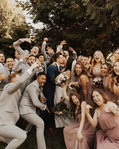 a large group of people standing around each other in front of some trees and bushes