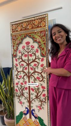 a woman standing next to a large painting on the side of a wall in front of a potted plant