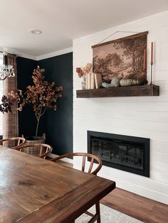 a dining room table and chairs in front of a fireplace with a painting on the wall