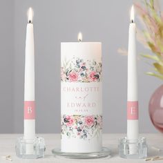 three candles with personalized labels on them sitting next to a vase and flower arrangement