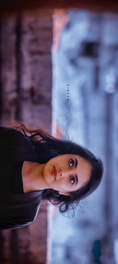 a woman with long black hair standing in front of a brick wall and looking at the camera