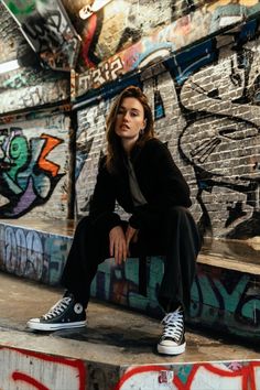 a woman sitting on the edge of a graffiti covered wall