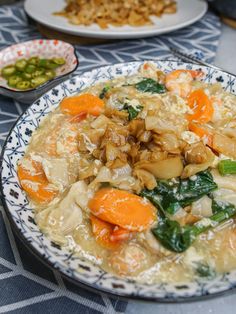 a bowl of soup with carrots, spinach and other foods on the table