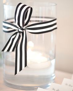 black and white striped ribbon tied around a clear glass filled with water, candles and cards