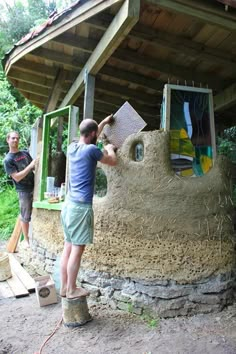 two men working on a sand sculpture in front of a building that has been built into the ground