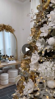 a white christmas tree with gold and silver ornaments in front of a mirror on the wall