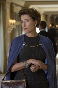 a woman in a black dress and blue jacket is walking down a hallway with other people