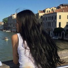 a woman standing on a bridge looking at boats in the water and buildings behind her