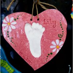 a pink heart shaped ornament with a baby's foot painted on it