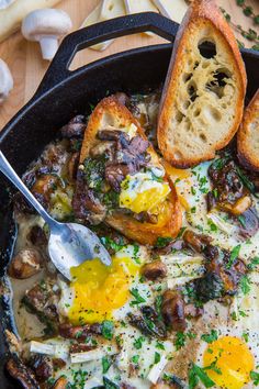 an iron skillet filled with eggs, mushrooms and bread on top of a wooden table