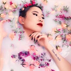 a woman laying in a bathtub with flowers all over her head and hands on the side