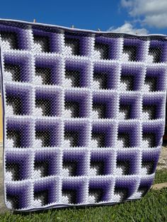 a purple and white crocheted blanket sitting in the grass