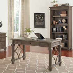 a desk with a laptop on it in front of a bookshelf and window