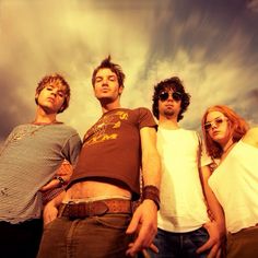 four people are standing in front of a cloudy sky and one person is wearing sunglasses