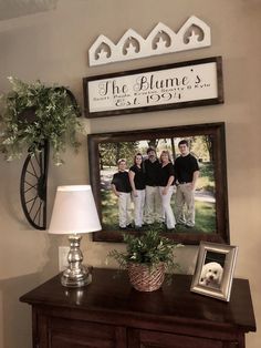 a family photo hanging on the wall above a dresser with a lamp and potted plant