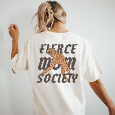 🐅Join the ranks of the fearless with our boho Fierce Mom Society Graphic Tee. Perfect for the edgy, strong, dynamic, and powerful women who shape the world, this shirt features a bold tiger graphic symbolizing strength and courage. Made for those who proudly lead their pack, it's more than just a shirt--it's a statement. The is the perfect oversized boho graphic tee for the mom you know and love! 🖤SHIRT MATERIAL Comfort Colors Unisex Shirt 100% Ring-Spun Cotton Printed using Direct To Garment style- Inks are printed directly into the fabric. Different sizing may effect placement of final design. Colors may differ slightly due to different user monitor and screen settings.  🏁SIZING Shirts are true-to-size for UNISEX RELAXED fit  Mockup photos are typically on sizes Medium & Large. Please Boho T-shirt, Oversize Tshirt Outfits, Trending Graphic Tees, Tiger Graphic, Cool Mom, Badass Women, Mom Tees, Tshirt Outfits, T Shirt Oversized