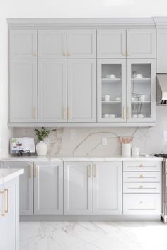 a kitchen with white cabinets and marble counter tops, gold trim on the door handles