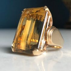 14k Stamped & tested yellow gold cast Citrine Quartz statement ring with a bright polish finish. This contemporary art-deco style fashion ring features a top center four- prong basket head-set emerald-shape step-cut citrine quartz with layered rolling cathedral shoulders. Ring measures approximately 20.00mm at the base of the top and approximately 9.50 wide at the wildest point of each shoulder tapering to approximately 2.78mm wide at the bottom of the shank. Ring size is: 5 3/4 Containing: One prong set emerald step cut natural citrine quartz. Measuring 24.00 x 17.50 x 11.66mm, (depth set). Approximate weight of 35.17ct, Clarity is eye clean, medium light, moderately strong, organgy yellow color, very good cut. Total Weight of Colored Stones:  36.17ct Total Weight of Ring:  16.28grams *20 Luxury Gold Faceted Rings, Luxury Yellow Gold Crystal Ring With Center Stone, Luxury Yellow Gold Timeless Crystal Ring, Luxury Timeless Yellow Gold Crystal Ring, Luxury Gold-tone Metal Ring, Luxury Yellow Gold Emerald-cut Crystal Ring, Luxury Faceted Yellow Gold Rings, Citrine Ring Engagement, Dream Rings