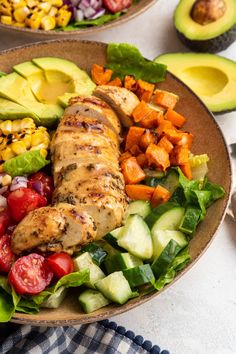 a salad with chicken, avocado, tomatoes, corn and cucumbers