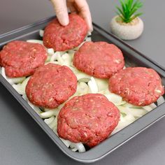 a person placing hamburger patties on top of onions in a baking pan with sauce