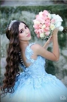 a beautiful young woman in a blue dress holding a bouquet of flowers and wearing a tiara