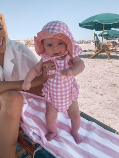 a woman sitting on top of a towel next to a small baby in a pink and white dress