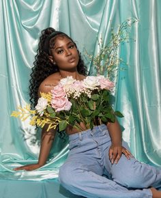 a woman sitting on the ground with flowers in her hand and wearing light blue jeans