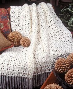 a white crocheted blanket sitting on top of a couch next to a pillow