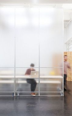 two people sitting on a bench in front of a wall with slats covering it