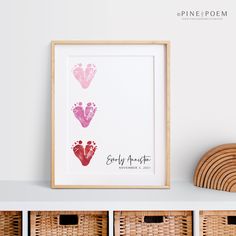 three baby footprints in pink and red are displayed on a shelf next to wicker baskets