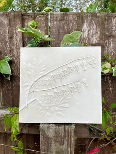 a sign that is on top of a wooden fence in front of some plants and flowers