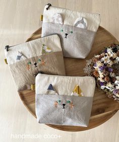 four handmade pouches with cats on them sitting on a wooden table next to flowers