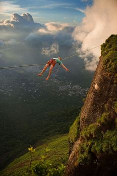 a woman is hanging from a rope above the ground while she climbs up a mountain