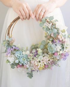 a woman holding a wreath with succulents and greenery in her hands