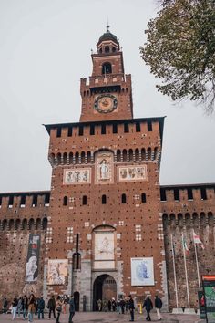 a tall brick building with a clock on it's face and people walking around