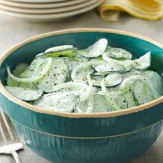 a green bowl filled with cucumbers on top of a table next to silverware