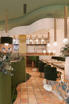 the interior of a restaurant with green chairs and plants on the counter area, along with tiled flooring