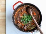 a pot filled with stew and carrots on top of a table next to a cutting board