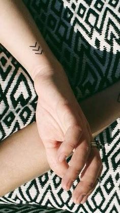 two hands holding each other over a black and white rug with an arrow tattoo on it