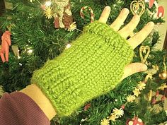 a person wearing green knitted mitts next to a christmas tree