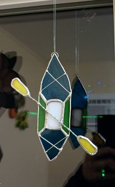 a stained glass light fixture hanging from the ceiling in front of a window with green and yellow accents