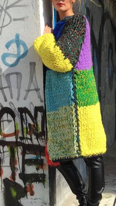 a woman is leaning against a wall wearing a colorful sweater and black leather leggings