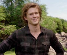 a young man smiles while standing in front of some rocks and trees with his hands on his hips