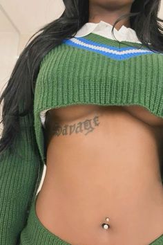 a woman with tattoos on her stomach wearing a green sweater