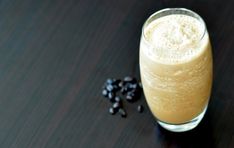 a glass filled with liquid sitting on top of a table next to some black beans