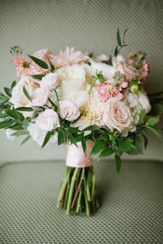 a bouquet of pink and white flowers sitting on a green couch next to a pillow