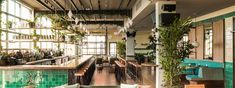 the inside of a restaurant with tables, couches and plants hanging from the ceiling